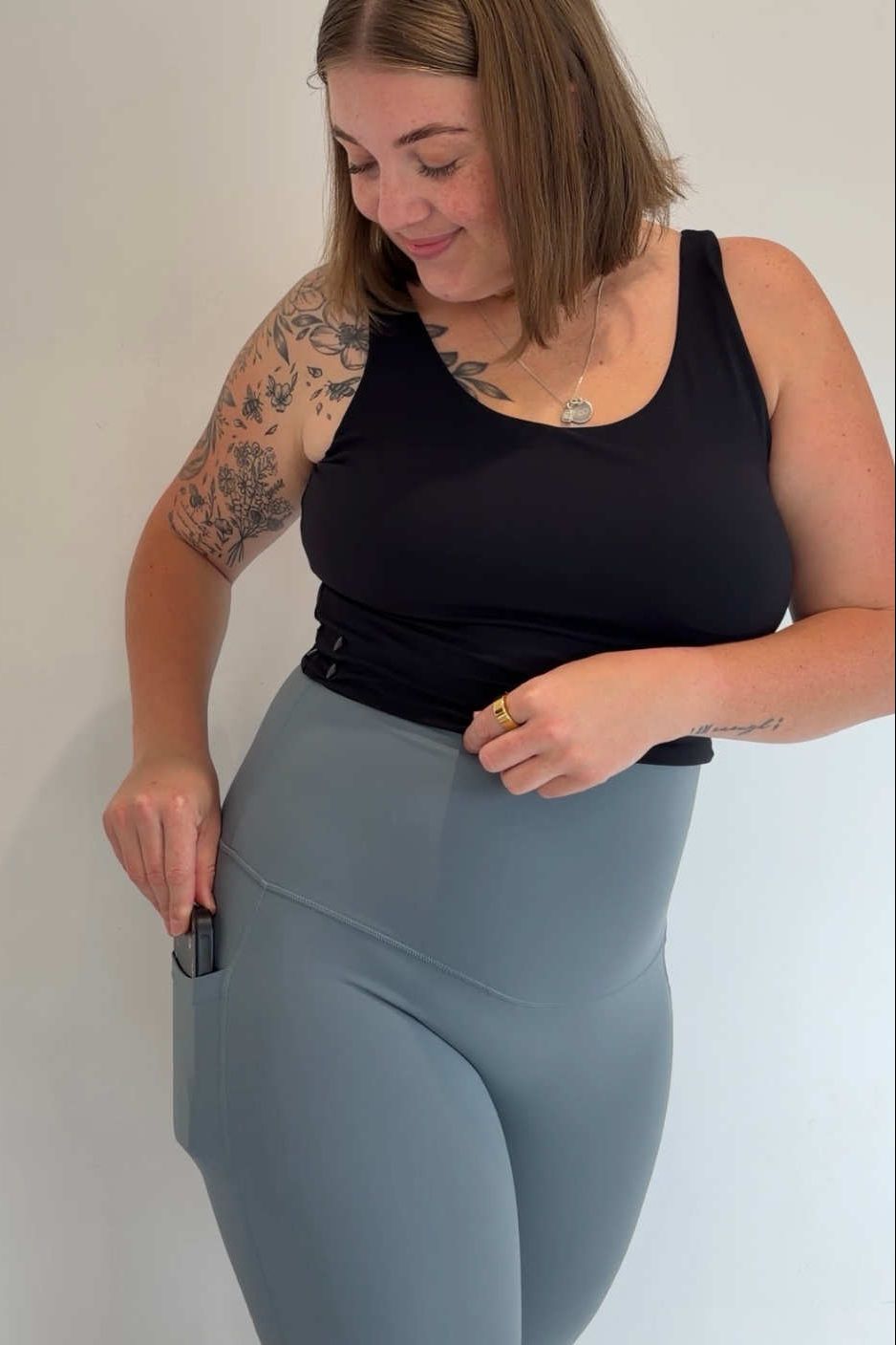 Woman wearing a black tank top and gray leggings against a plain background