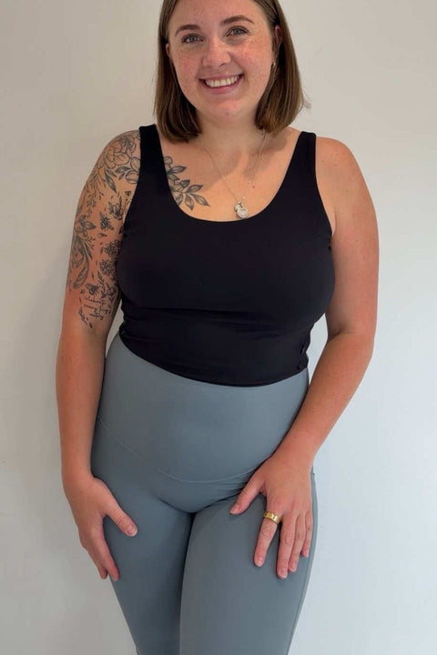 Woman wearing a black tank top and gray leggings against a white background