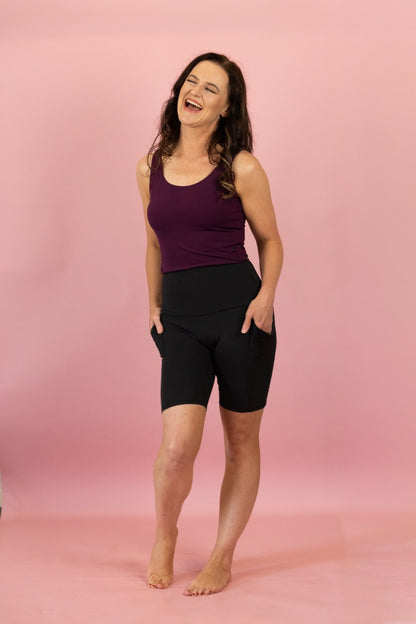 Woman wearing a purple tank top and black shorts on a pink background