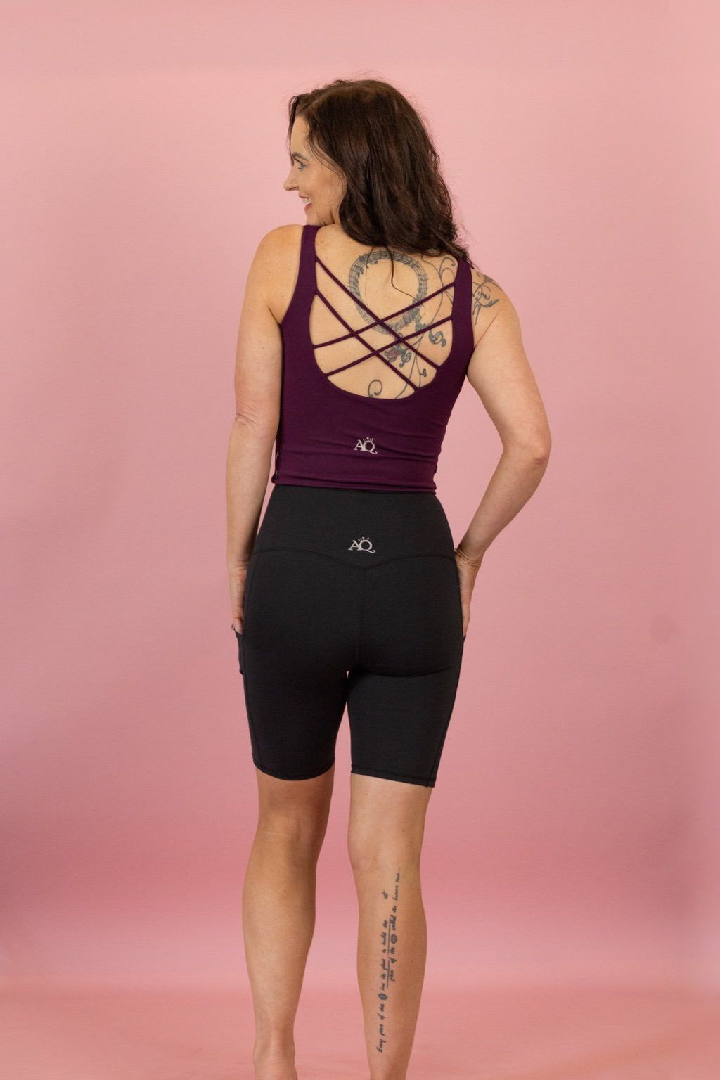 Woman wearing a purple tank top and black shorts on a pink background