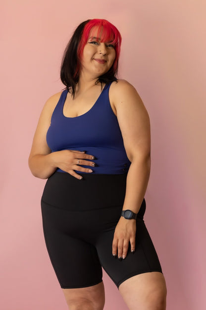 Woman wearing a blue tank top and black shorts against a pink background